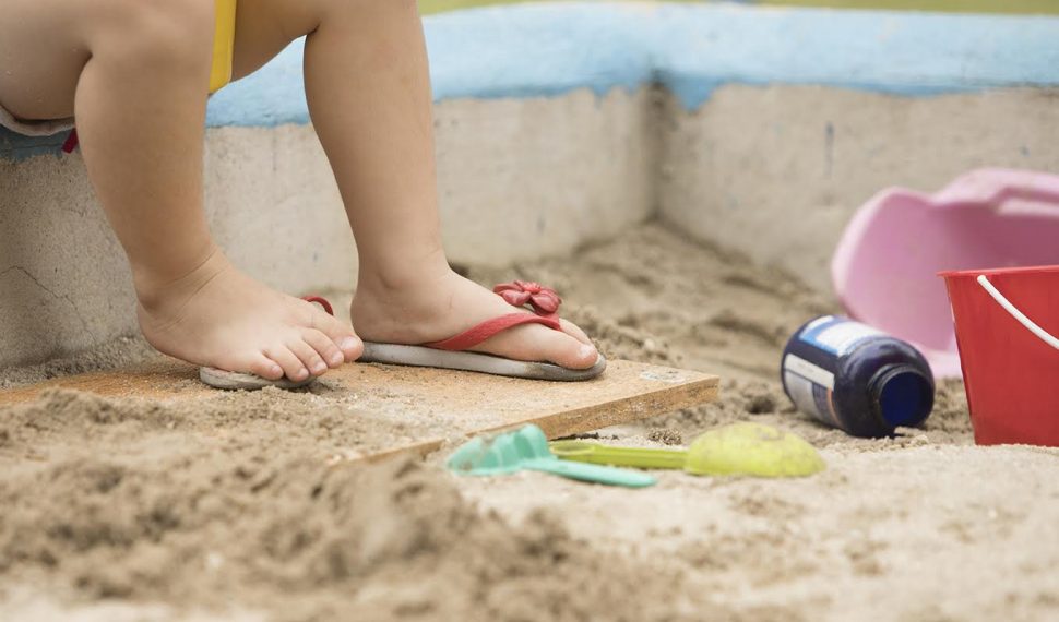 pezinhos de criança com chinelo de dedo em um tanque de areia com brinquedos